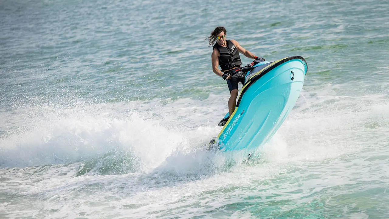 Man standing up on a moving yellow and turquoise jet ski